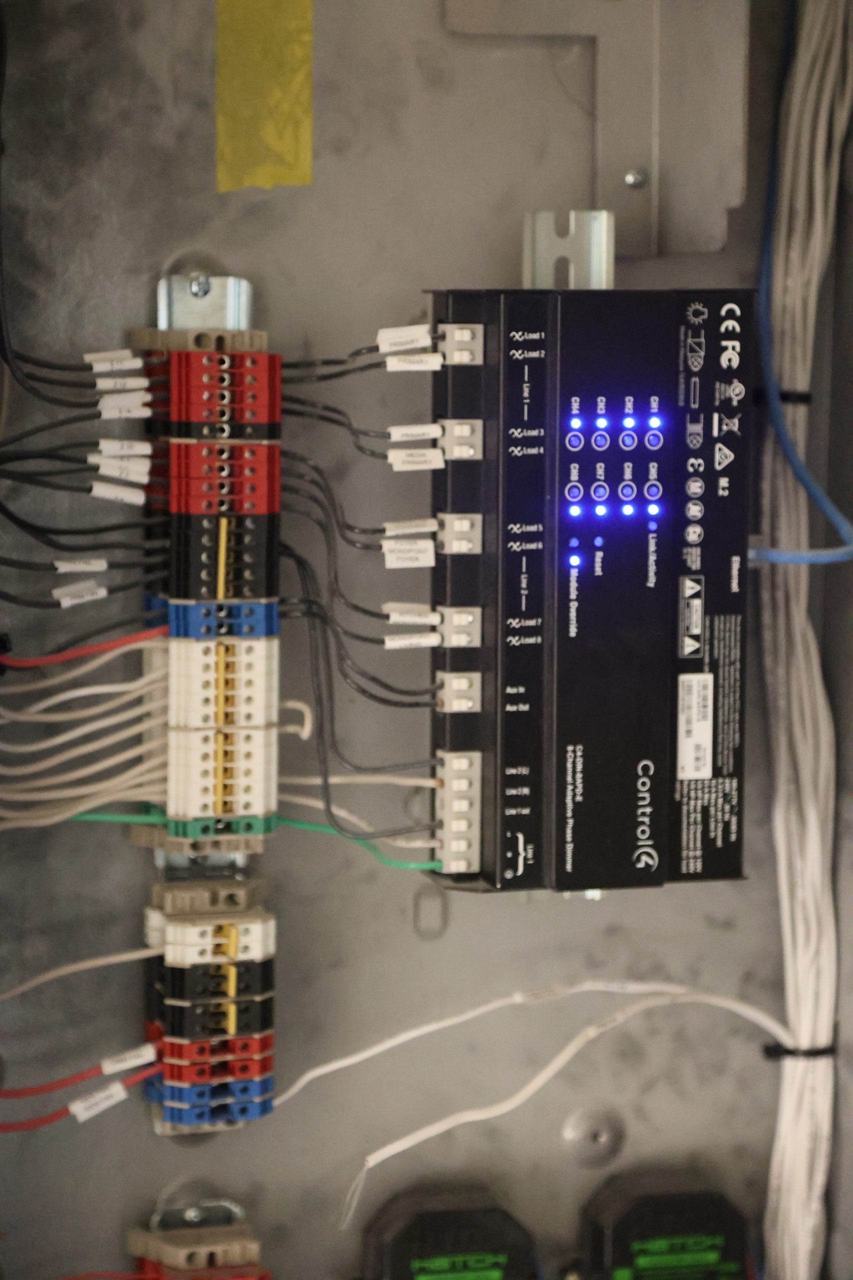 Control4 lighting control module installed inside an electrical panel, showing organized wiring, labeled connections, terminal blocks, and illuminated status LEDs.