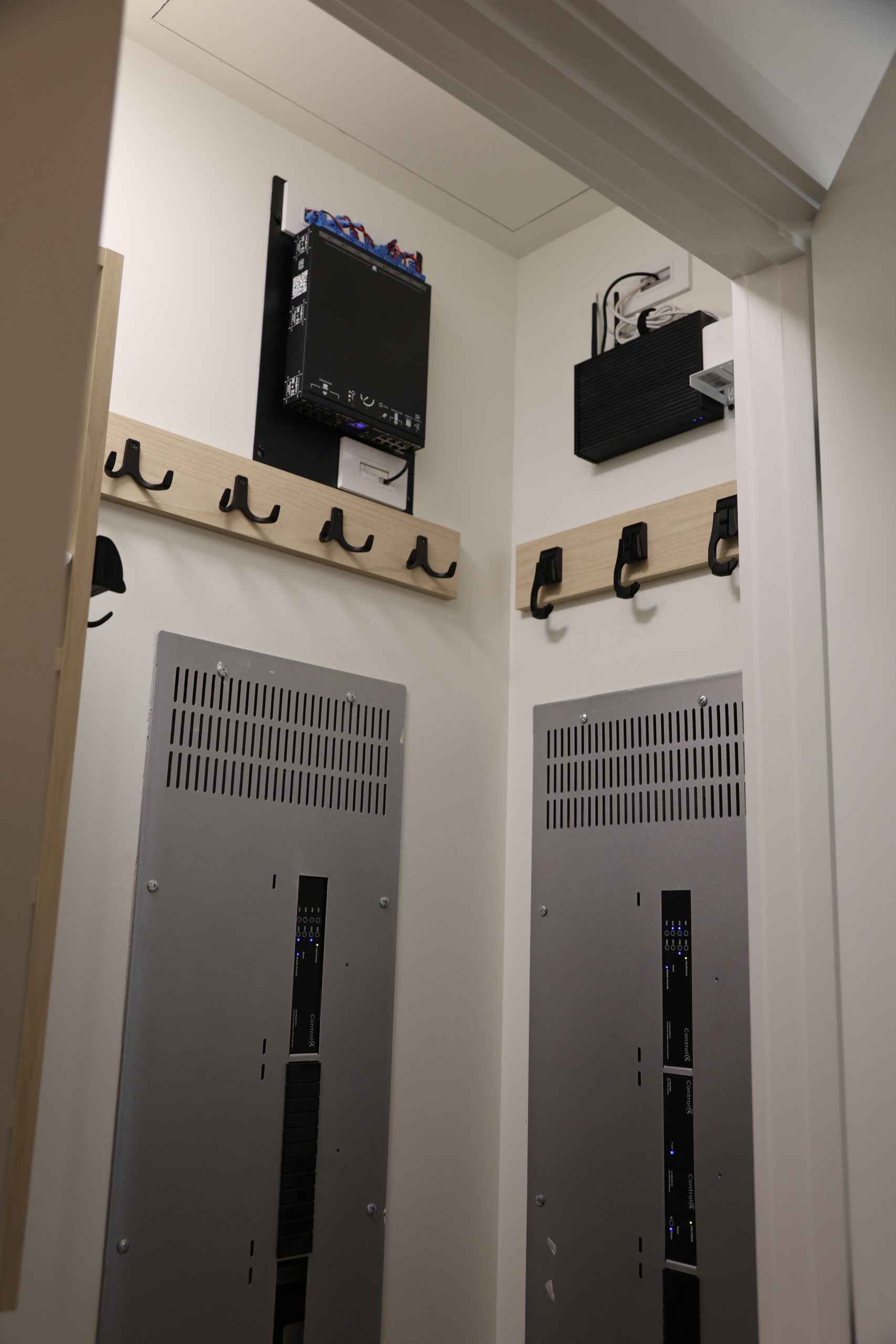 Utility closet with two wall-mounted electrical panels, network equipment, and wooden coat hooks beneath a sloped ceiling.