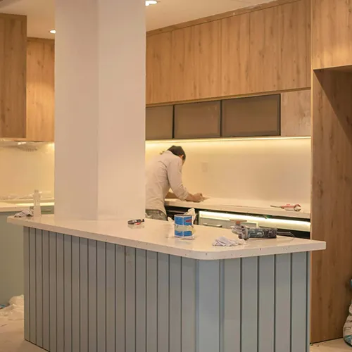 Residential electrician installing wiring and under-cabinet lighting in a modern, newly remodeled kitchen.