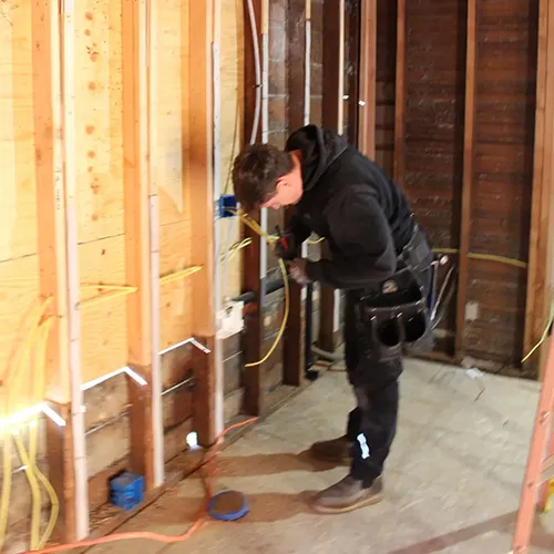 Residential electrician roughing in new electrical wiring through exposed wooden wall studs during a home renovation project.