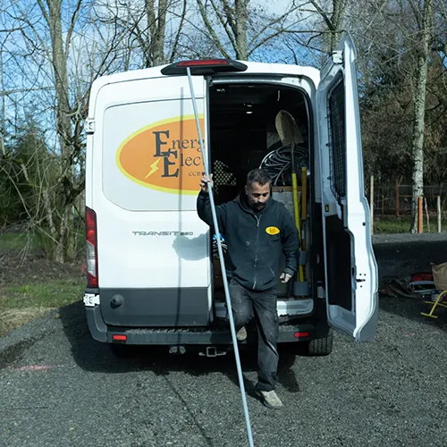 Energized Electric LLC technician stepping out of a fully equipped company work van carrying metal electrical conduit for a residential job.