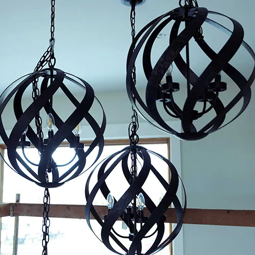 Three newly installed custom orb-style metal chandelier lighting fixtures hanging from chains in a residential home.